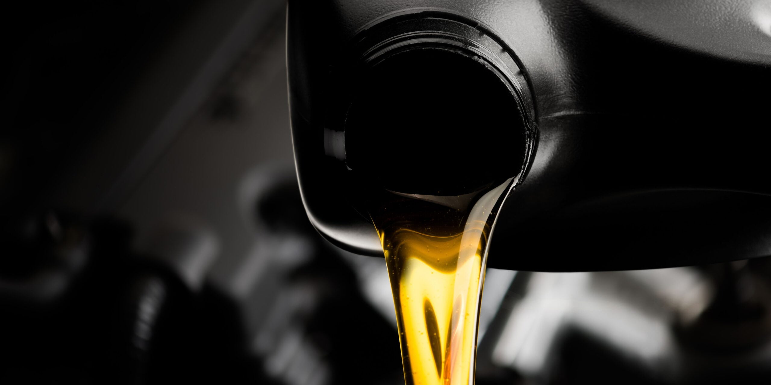Golden motor oil being poured from a black plastic container.